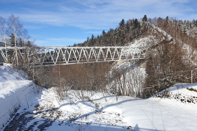 Snow covered plants by bridge against sky