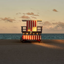 Lifeguard hut on beach against sky during sunset