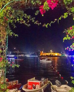 Boats moored in illuminated water against sky at night