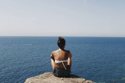 Rear view of woman sitting on sea against clear sky