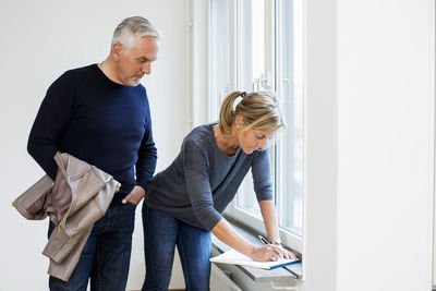 Mature businessman looking at female colleague writing on window sill at home