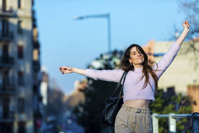 Portrait of woman with arms outstretched standing in city