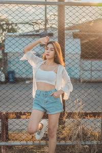 Full length of young woman standing by chainlink fence