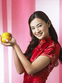 Portrait of smiling woman with oranges standing against backdrop