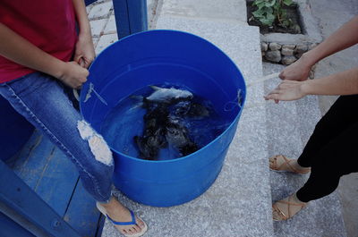 Low section of female friends carrying fish in blue bucket on steps