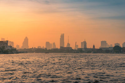 Sea by buildings against sky during sunset