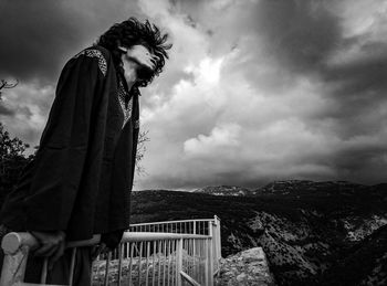 Side view of a man on landscape against cloudy sky