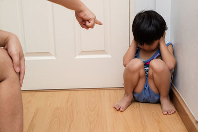 Woman pointing at boy sitting against door at home