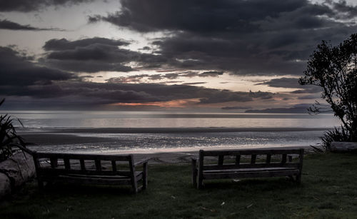 Empty bench on beach against sky during sunset