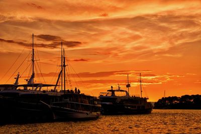 Sailboats moored on sea against orange sky