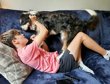 Teen boy playing with dog on a couch.
