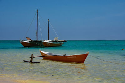 Sailboats moored on sea against blue sky