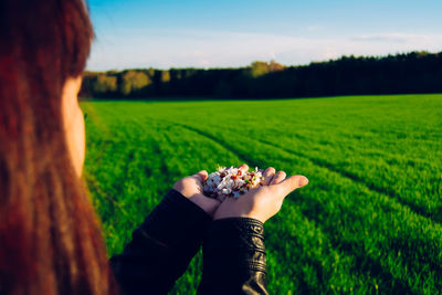 Rear view of a young woman with flowers in hand outstretched on field