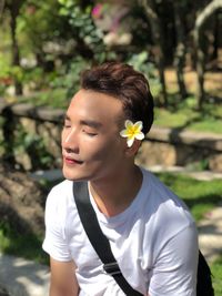 Young man with flower on ear sitting in park during sunny day
