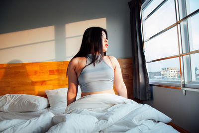 Young woman sitting on bed at home