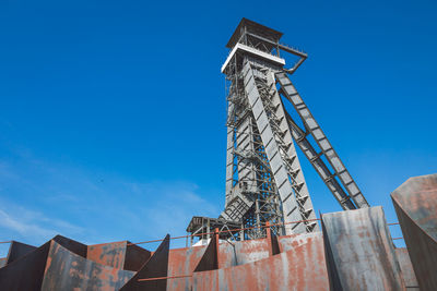 Low angle view of crane by building against clear blue sky