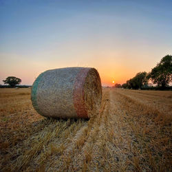 Hay bales on field against sky during sunset