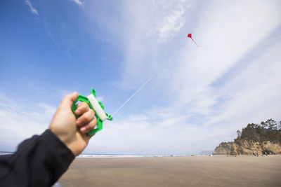 Person holding kite flying over beach against sky