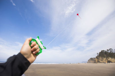 Human hand holding on to red kite at the beach.