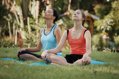 Women meditating while sitting on field at park