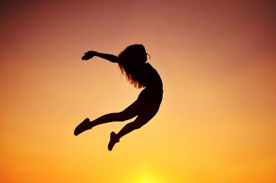 Low angle view of silhouette girl jumping against clear sky during sunset