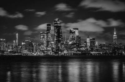 Illuminated buildings by river against sky at night