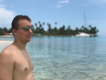 Smiling shirtless man wearing sunglasses at beach