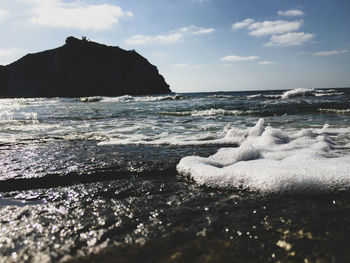 Waves rushing towards shore against sky