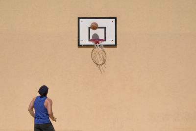 Rear view of man playing basketball against wall