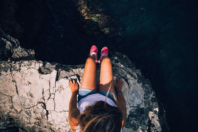 Low section of woman sitting on rock by sea