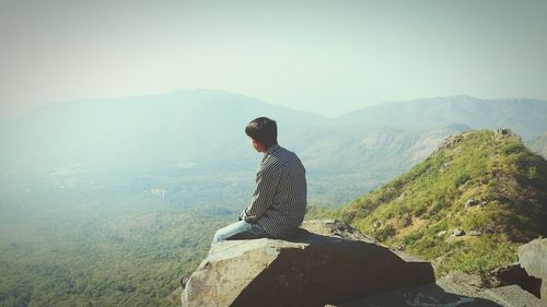 Rear view of woman sitting on mountain against sky