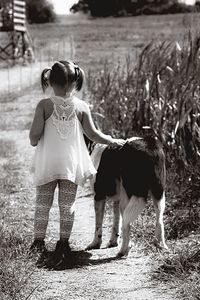 Rear view of girl walking with dog on footpath by plants