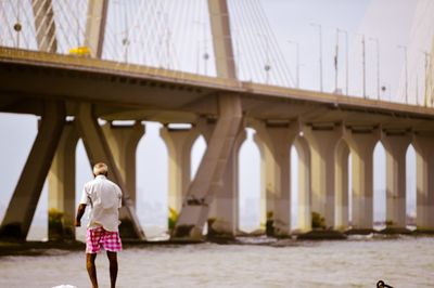 Rear view of man standing against bridge over river