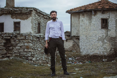 Portrait of man standing outside house against sky