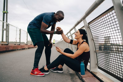 Cheerful male and female athletes holding hands during sports training on footbridge