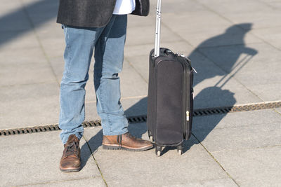 Low section of man with suitcase standing on tiled floor