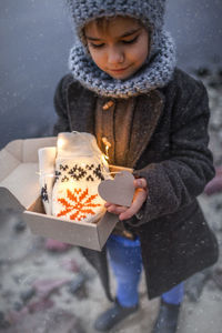 Pretty girl in knitted grey hat opening a crafted gift box with a new pair of gloves, snowfall