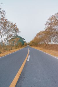 Empty road by trees against clear sky