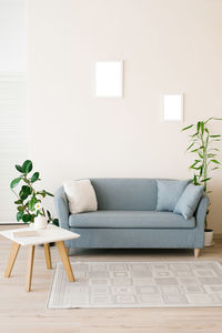 A dusty blue sofa with pillows, a white coffee table, potted plants in a bright cozy living room