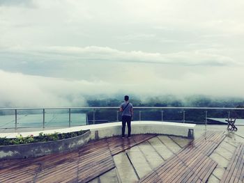 Rear view of man standing by railing against sky