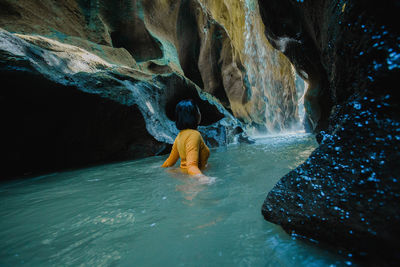 Rear view of man surfing on rock