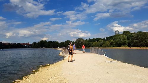 Rear view of woman walking on river by city against sky