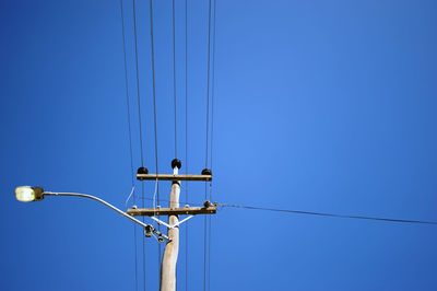 Low angle view of electricity pylon against clear blue sky during sunny day