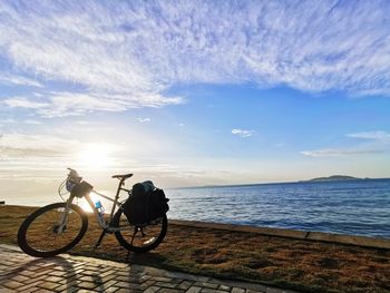 Bicycle on beach against sky during sunset