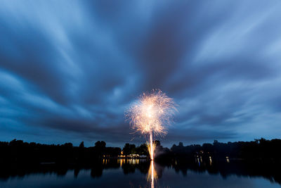 Firework display over lake against sky at night