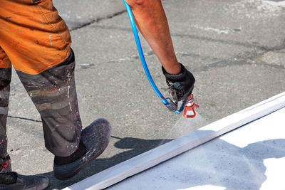 A road worker in dirty overalls, bending over the asphalt, applies white road markings 