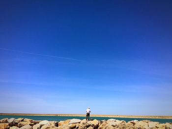 Rear view of man standing at beach against clear blue sky