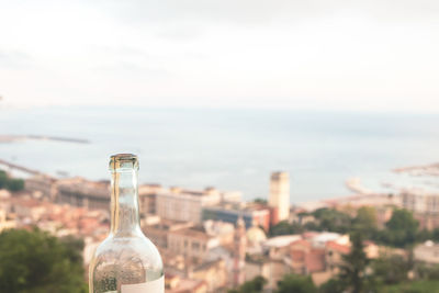 Close-up of wine bottle by sea against cityscape