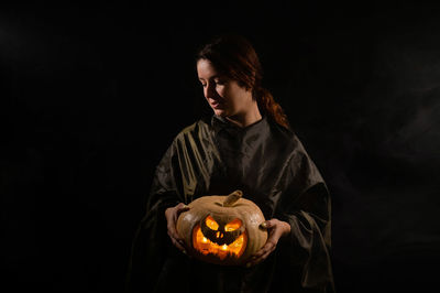 Man holding pumpkin while standing against black background