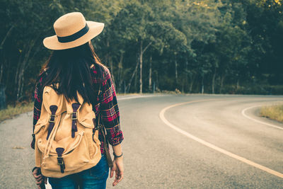 Rear view of woman standing by road against trees